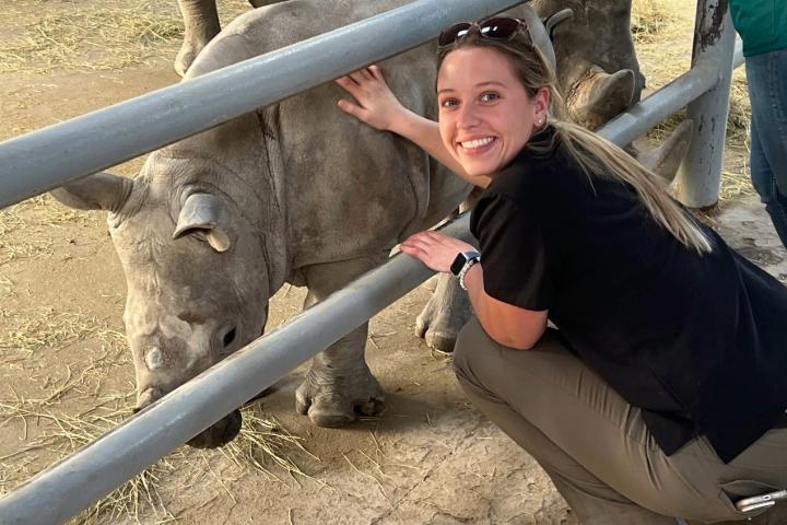 Erica smiling while squatting down in front of a rhino, touching it through a fence.