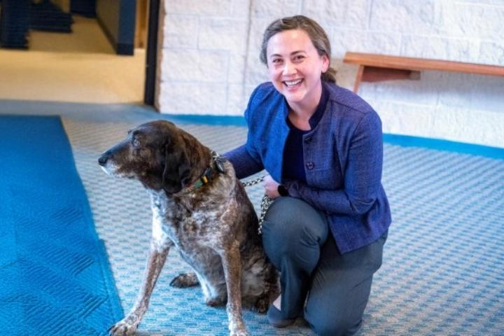 Jennifer is kneeling on a blue carpet smiling. Next to her is a German Shorthaired Pointer dog.